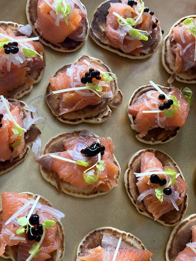 Vue rapprochée de canapés au saumon et aux jeunes pousses, alignés sur un plateau.