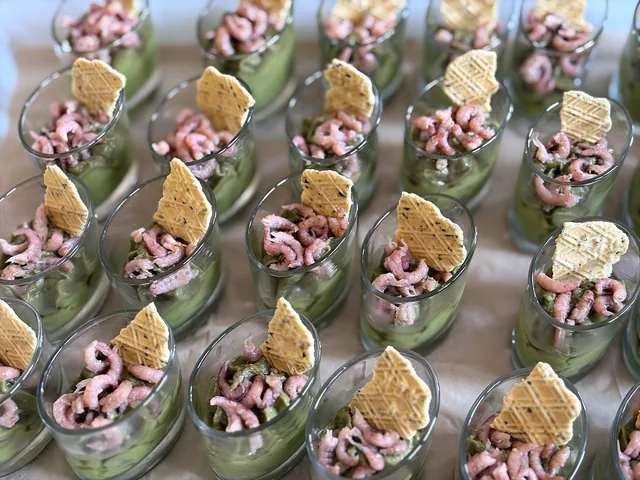 Verrines de crème verte garnies de crevettes et d’une tuile dorée.