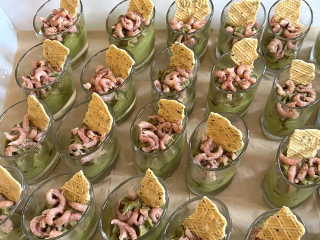 Verrines aux crevettes alignées sur un plateau, avec une crème verte et des tuiles dorées.